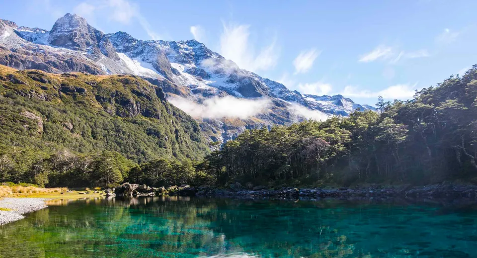 Un tranquillo lago alpino con montagne innevate e piante verdi si riflette nelle acque limpide vicino al Nayland College.