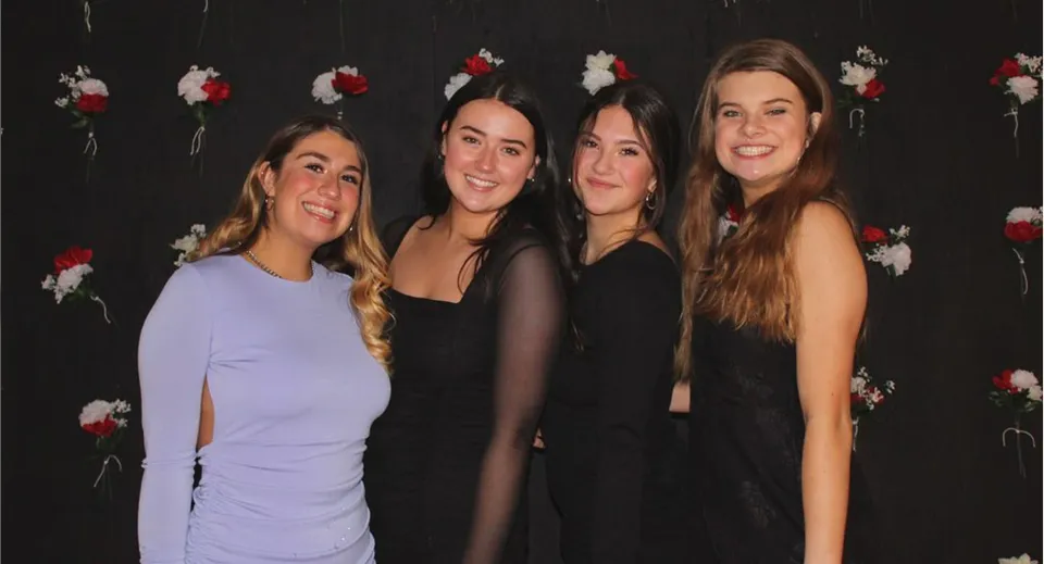 Quattro studentesse con lunghi capelli scuri sono in piedi davanti a uno sfondo nero con motivi floreali rossi e bianchi nel campus delle Seattle Public Schools.
