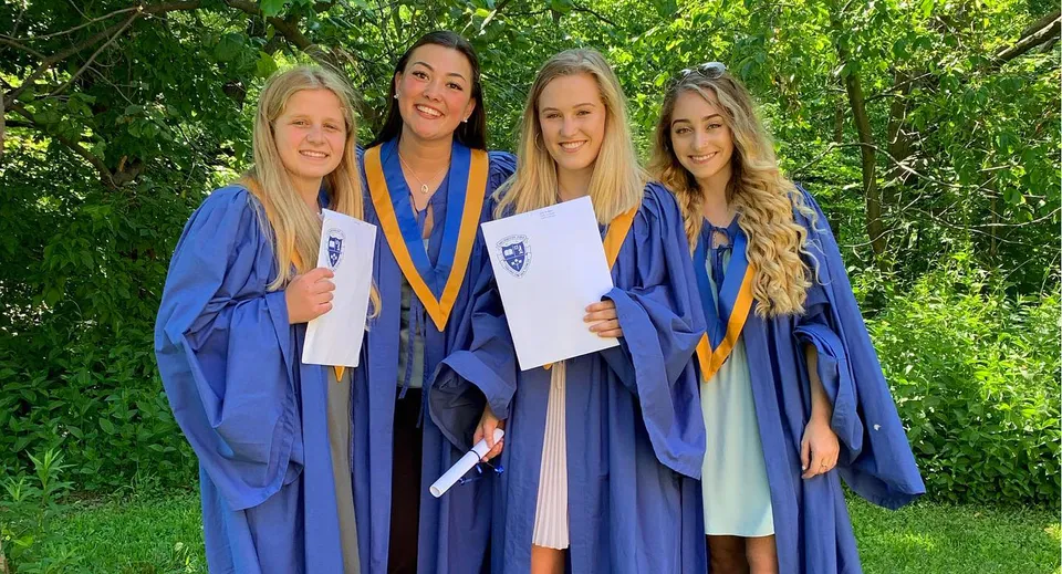 Quattro studentesse in toga blu da diploma si trovano insieme nel verde del campus del Birchmount Park Collegiate Institute.