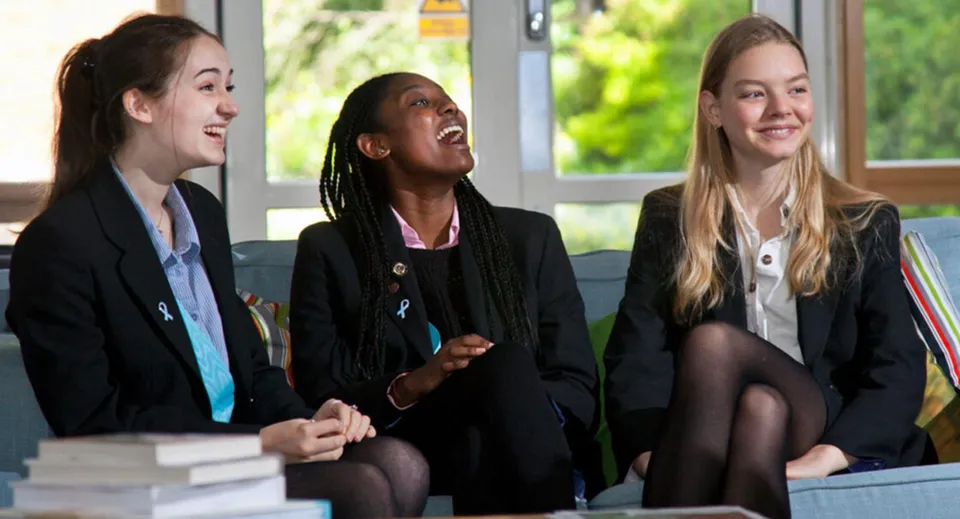 Tre studentesse della Woldingham School sono sedute insieme e chiacchierano davanti a una luminosa finestra.