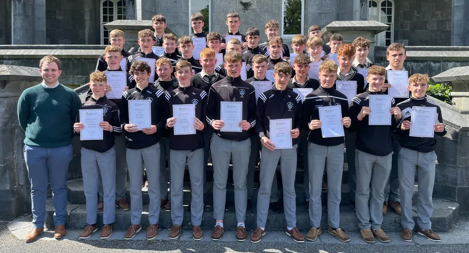 Un gruppo di studenti del St. Kieran’s College si trova davanti a un edificio scolastico tenendo con orgoglio i propri certificati.