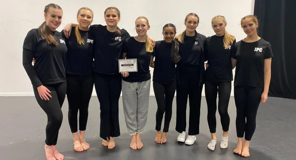 Un gruppo di studentesse del John Paul College indossa uniformi nere e posa insieme in uno studio.
