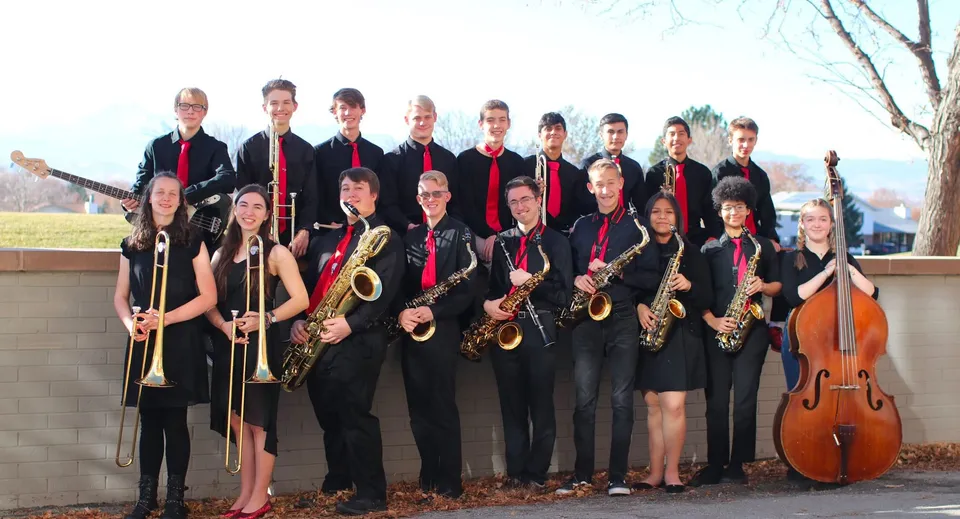 Un gruppo di musicisti in abiti formali posa con i propri strumenti davanti a un edificio del campus delle St. Vrain Valley Schools.