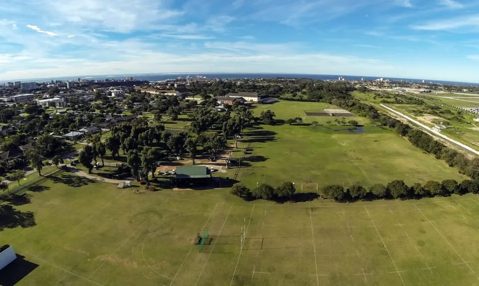 Un grande campo verde con alberi sparsi davanti allo skyline della città è visibile vicino alla Victoria Park High School.