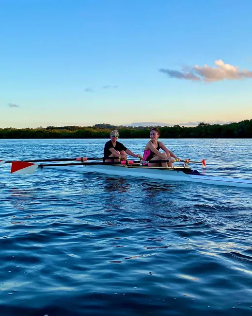 Dos chicas remando en una embarcación de remo sobre aguas tranquilas al atardecer