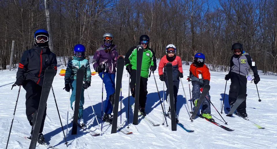 Un gruppo di studenti del Bishopstrow College si trova con abiti invernali colorati su un sentiero nel bosco innevato sotto un cielo azzurro.