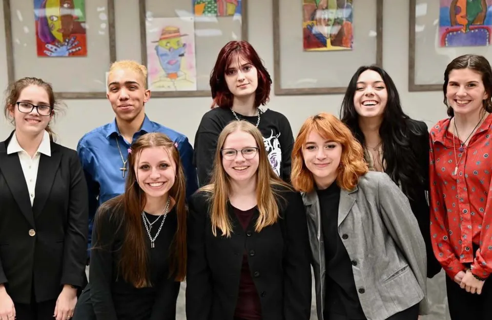 Un gruppo di studentesse in piedi insieme in uno spazio interno del campus della Athens Christian School davanti a un'opera murale colorata.