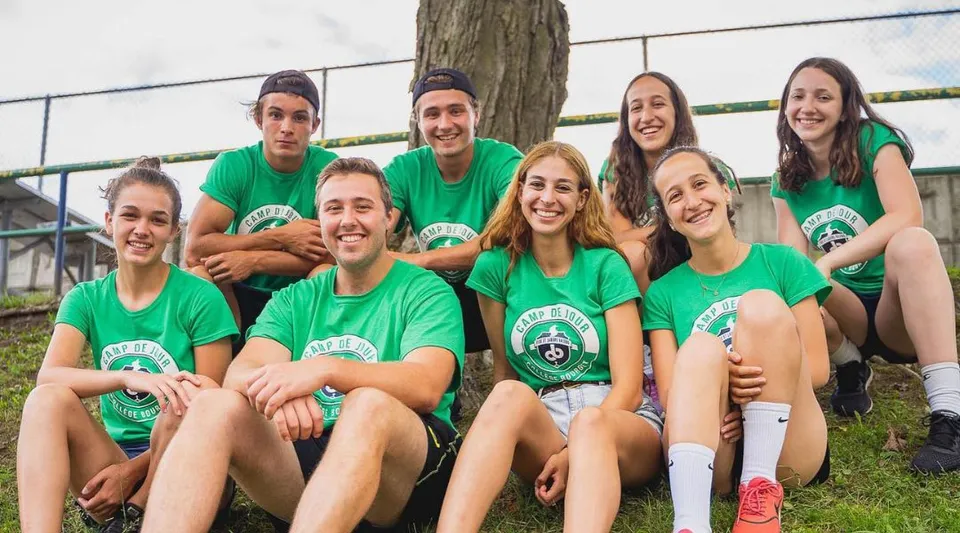 Un gruppo di studenti del College Bourget siede insieme all'aperto sorridendo davanti a uno sfondo di legno.