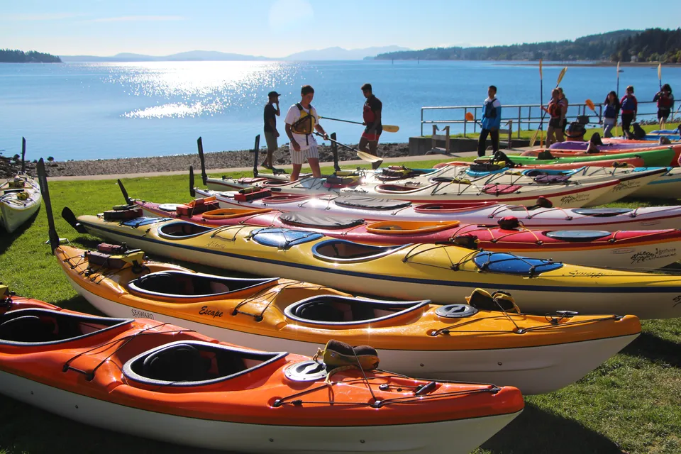 Kayak e canoe giacciono sulla riva di un lago nel terreno della Ladysmith Secondary School davanti alle montagne.