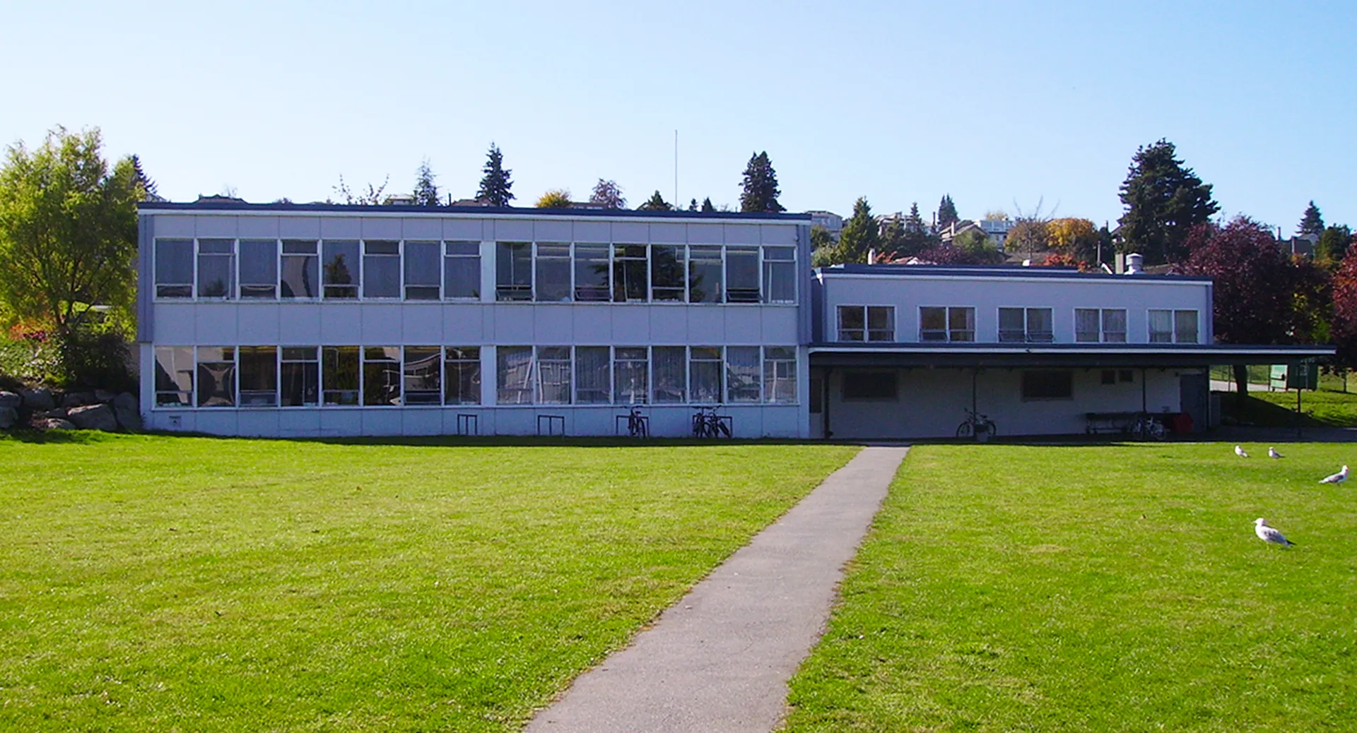 L'edificio moderno in vetro della Prince of Wales Secondary School si trova su un prato verde sotto un cielo azzurro.