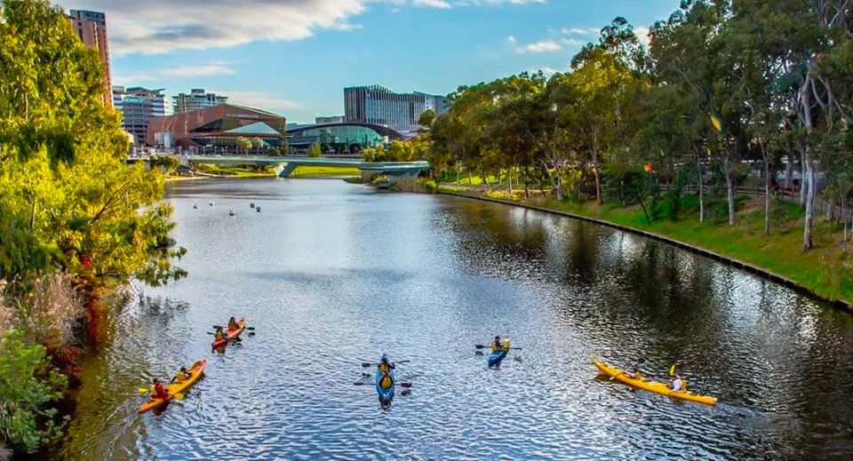 Studenti della Golden Grove High School pagaiano in kayak e canoa su un corso d'acqua calmo con uno sfondo urbano moderno.