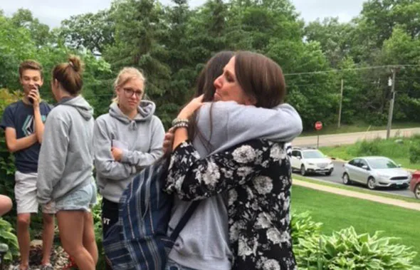 Una mujer con blusa estampada abraza a una chica con mochila al aire libre