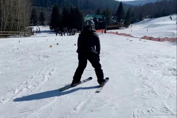 Persona de espaldas esquiando en una pista cubierta de nieve con árboles al fondo