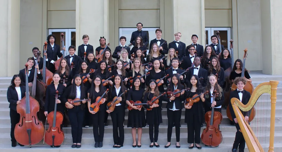 Un grande gruppo di musicisti in abito formale si trova davanti a un edificio in stile classico nel campus di Embley.