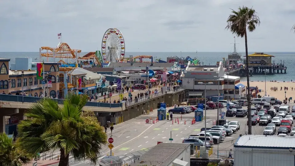 Studenti del Santa Monica College camminano lungo il vivace boardwalk con la ruota panoramica e le attrazioni del parco divertimenti sul mare.