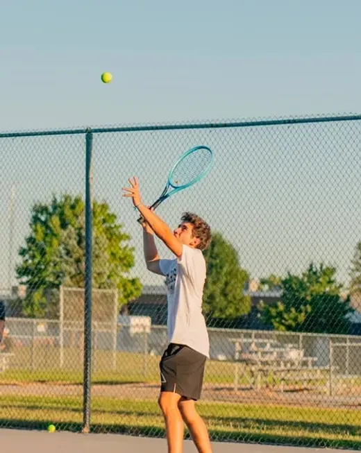 Studente al servizio durante una partita di tennis su un campo all'aperto negli USA