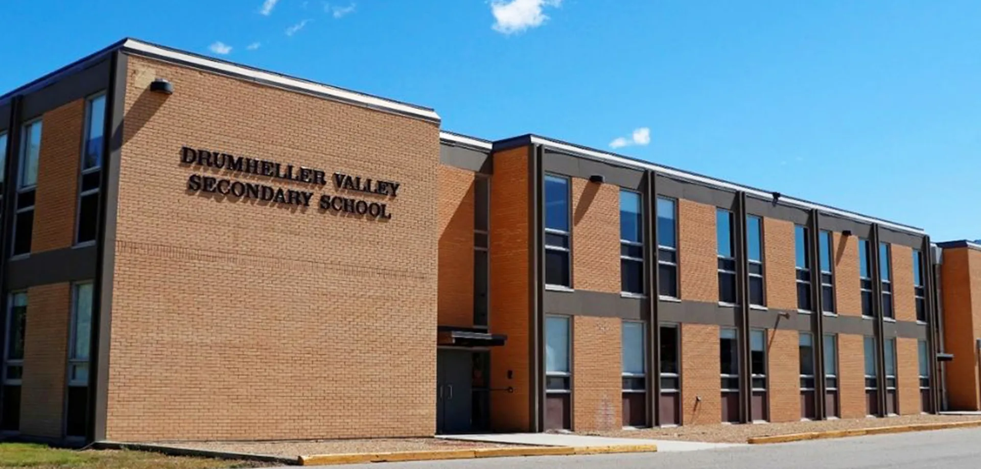 L'imponente edificio in mattoni della Drumheller Valley Secondary School si erge sotto un cielo azzurro nuvoloso.