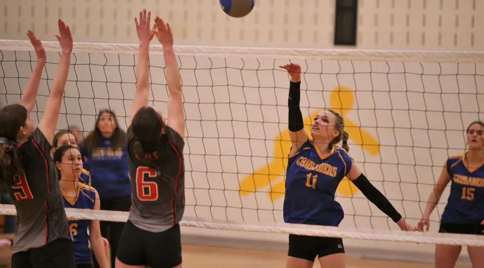 Una giocatrice di pallavolo della Char-Lan District High School schiaccia la palla a rete contro due avversarie a muro.