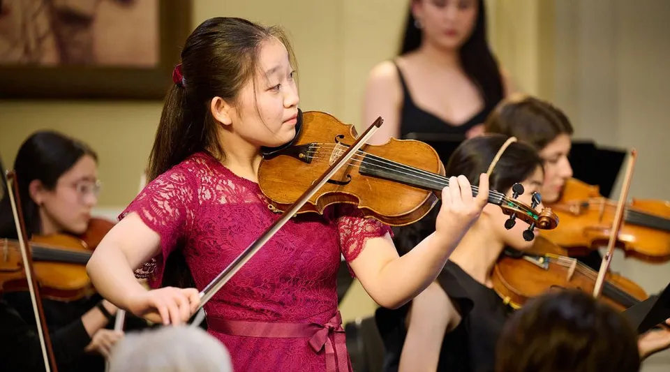 Una studentessa della Walnut Hill School for the Arts suona il violino sul palco insieme ad altri musicisti.