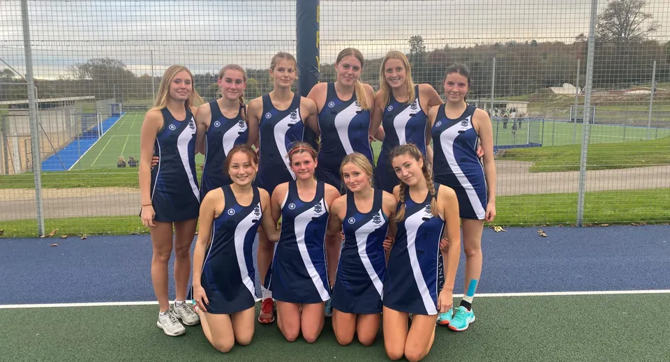 Un gruppo di giovani atlete sta insieme sul campo sportivo del Templemichael College con una recinzione e alberi sullo sfondo.