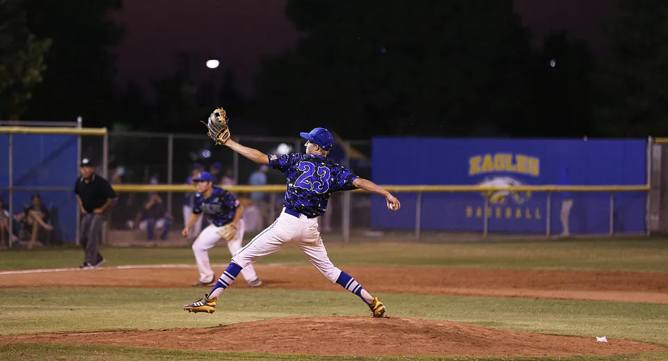 Un giocatore di baseball della Bakersfield Christian lancia la palla sul campo di notte sotto i riflettori.