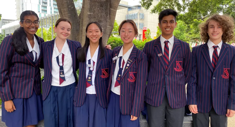 Un gruppo di studenti della Brisbane State High School si trova davanti a uno sfondo urbano alberato.