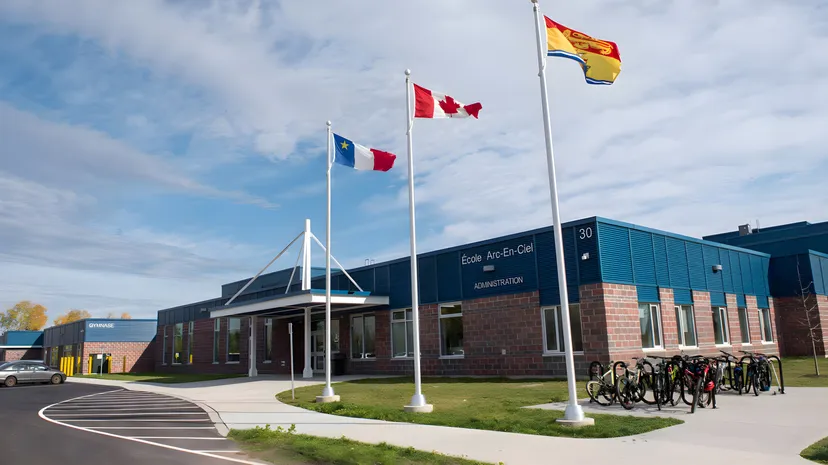 L'edificio della École Arc-en-ciel mostra le bandiere del Canada e della Spagna davanti a un'area pavimentata con rastrelliere per biciclette.