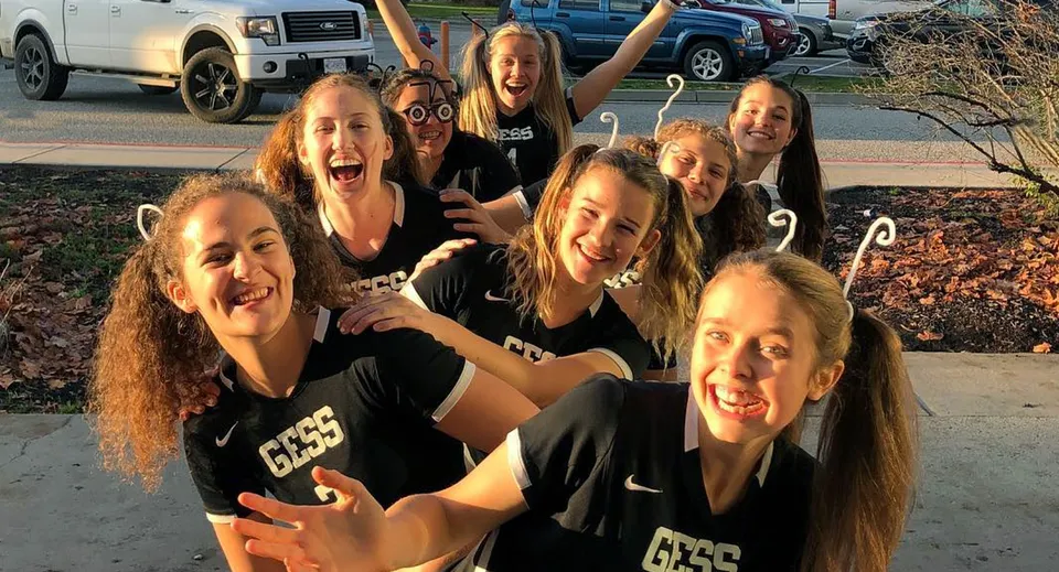 Un gruppo di studentesse della George Elliot Secondary School posa sorridendo all'aperto davanti a veicoli parcheggiati.