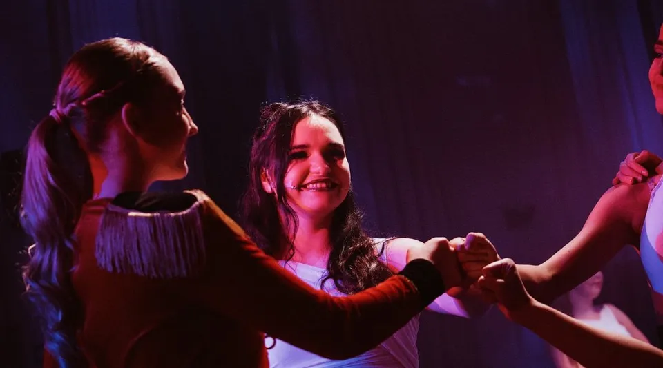 Due studentesse ballano insieme sul palco dell'Itchen Sixth Form College sotto luci di scena colorate.