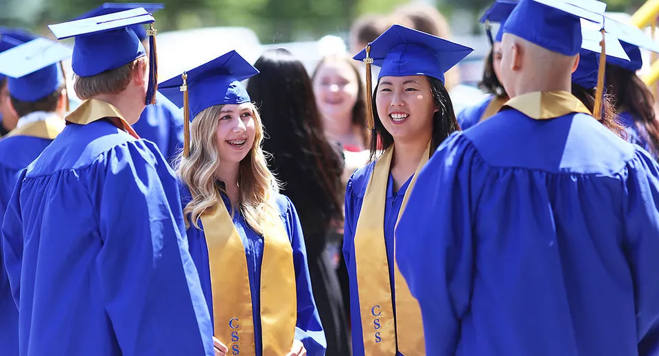 Un gruppo di diplomati della Chilliwack Secondary School posa insieme in toga e tocco blu davanti a uno sfondo verde.