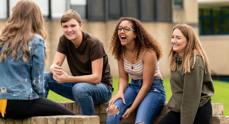 Un gruppo di studenti chiacchiera nell'area esterna del St. David’s College davanti a un edificio con uno spazio verde.