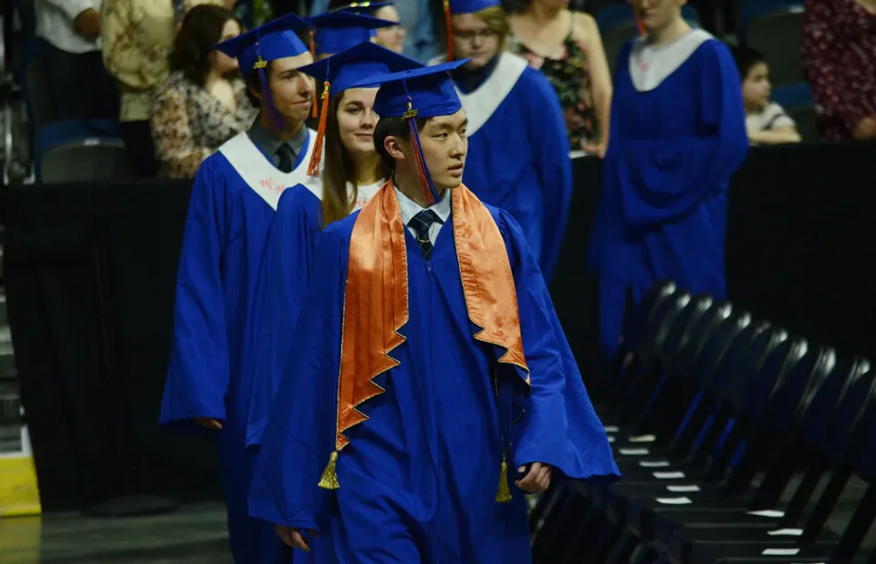 Studenti della Lethbridge School Division camminano in toga e tocco blu attraverso una sala.