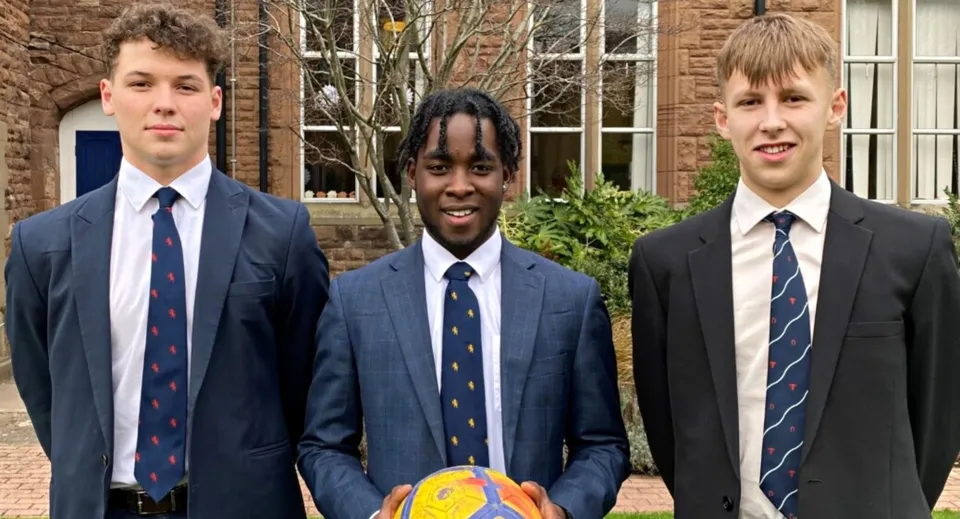 Tre studenti in divisa scolastica davanti a un edificio in mattoni nel campus del Blackrock College.