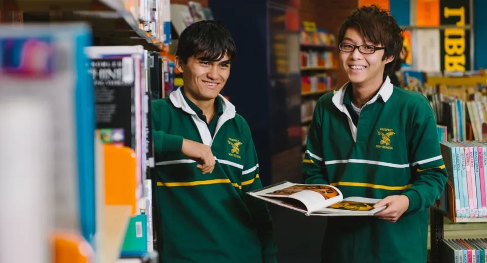 Due studentesse della Prospect High School si trovano nella biblioteca, una di loro tiene in mano un libro aperto.