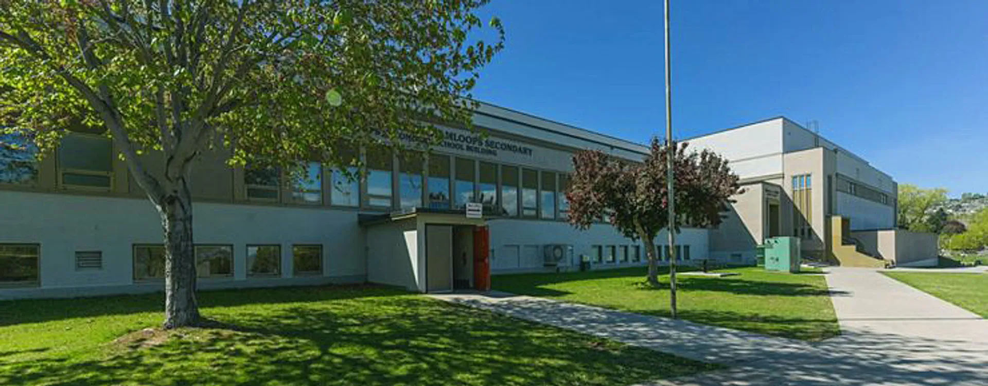 L'edificio moderno a più piani della South Kamloops Secondary School è circondato da una verde vegetazione e presenta grandi finestre.
