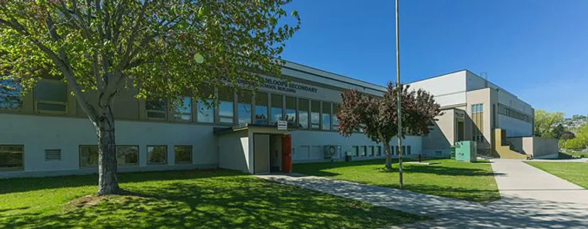 L'edificio moderno a più piani della South Kamloops Secondary School è circondato da una verde vegetazione e presenta grandi finestre.