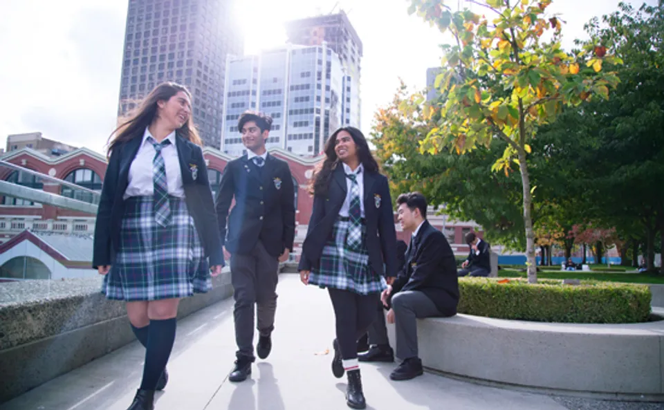 Un gruppo di studenti e studentesse della City Vancouver Academy High School cammina insieme nel campus scolastico tra alti edifici e alberi.