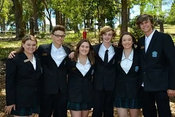 Un grupo de estudiantes de la Cardiff High School con uniformes escolares está en un bosque posando para una foto.