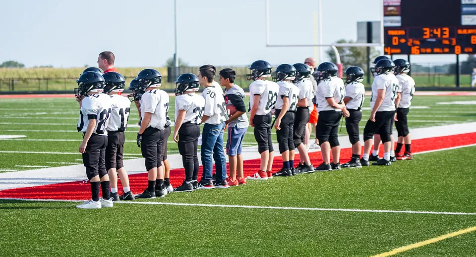 Un gruppo di giocatori di football in uniforme si trova sul campo di gioco alla Gilbert Public Schools davanti a un tabellone segnapunti.
