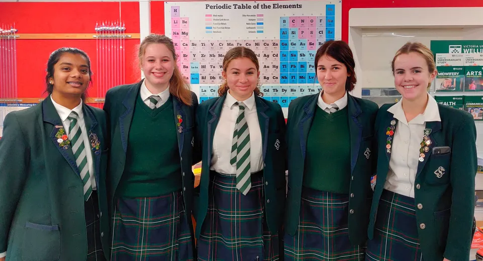 Cinque studentesse del Solway College sono in piedi davanti a una parete con la tavola periodica degli elementi.