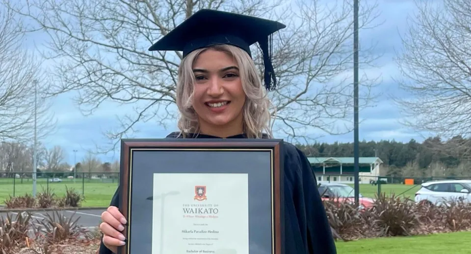 Una diplomanda con la toga da cerimonia tiene il suo diploma nel campus del Sacred Heart Girls' College a Hamilton e sorride.