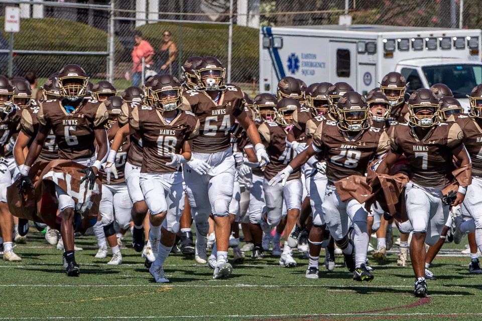 La squadra di football americano della Bethlehem Catholic School corre sul campo da gioco con le divise marroni.