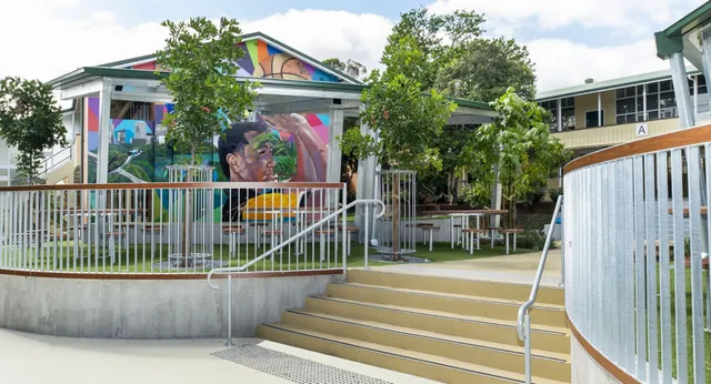 Il murales colorato sulla facciata della Yeronga State High School è circondato da un'area recintata con scale e una zona verde.