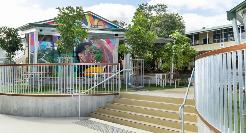 Il murales colorato sulla facciata della Yeronga State High School è circondato da un'area recintata con scale e una zona verde.