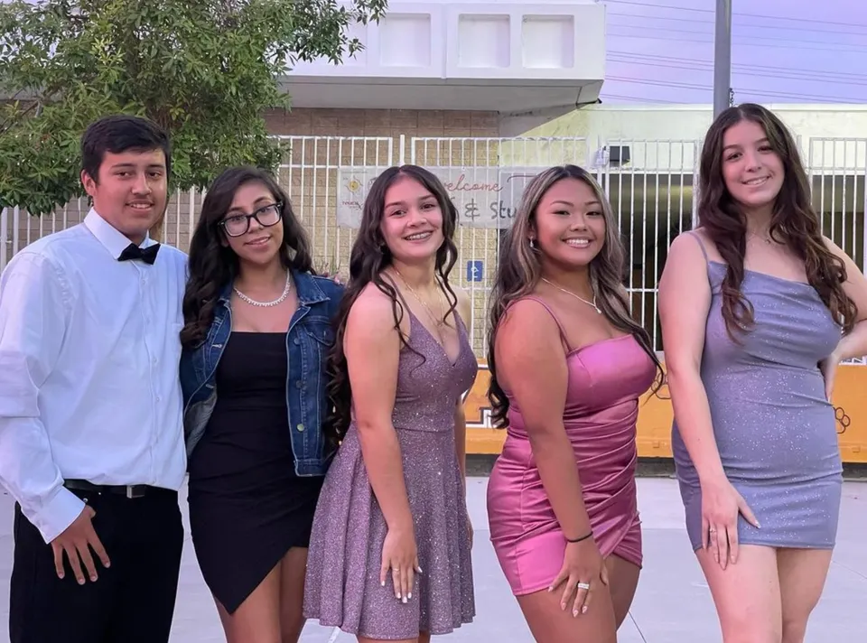 Un gruppo di studenti si trova davanti a un edificio con una recinzione metallica nel campus della John F. Kennedy High School.