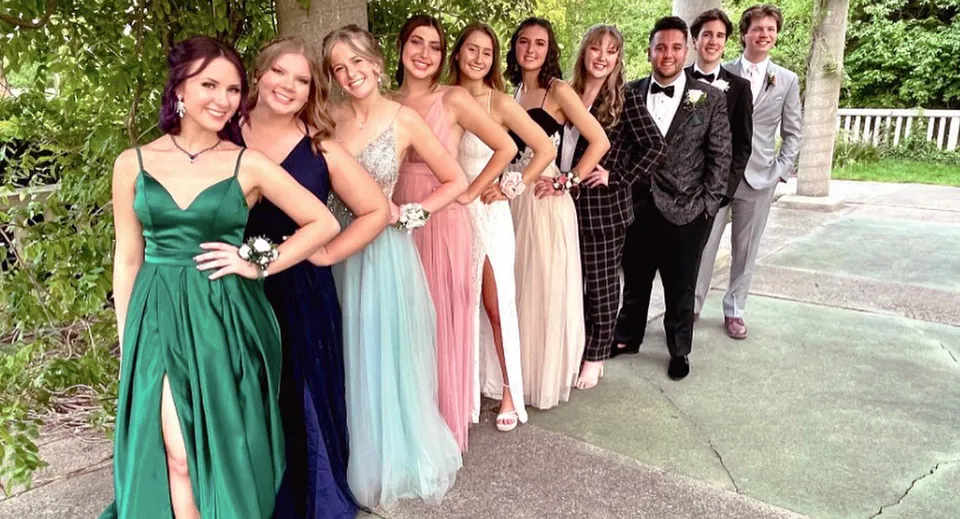 Un gruppo di persone vestite in modo elegante si trova insieme nell'area verde esterna della Lansing Catholic High School.