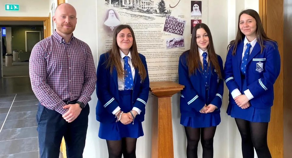 Un gruppo di studentesse e studenti si trova nel corridoio della Assumption Grammar School davanti a una bacheca informativa.
