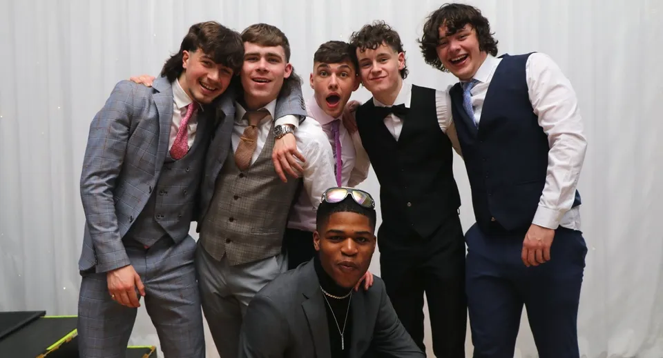 Sei studenti del St. Kieran’s College vestiti in abito elegante posano insieme sorridenti davanti a una tenda chiara.