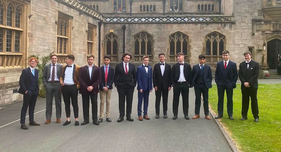 Un gruppo di uomini in abiti formali sta davanti all'edificio principale in stile gotico del Myddelton College.