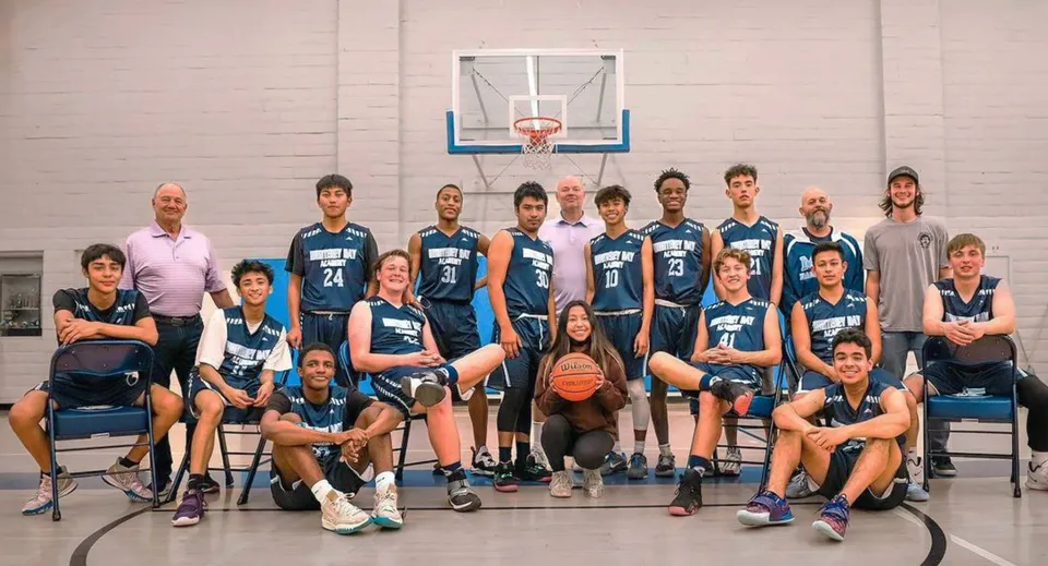Un gruppo di studenti della Monterey Bay Academy posa insieme nella palestra davanti a un canestro da basket.